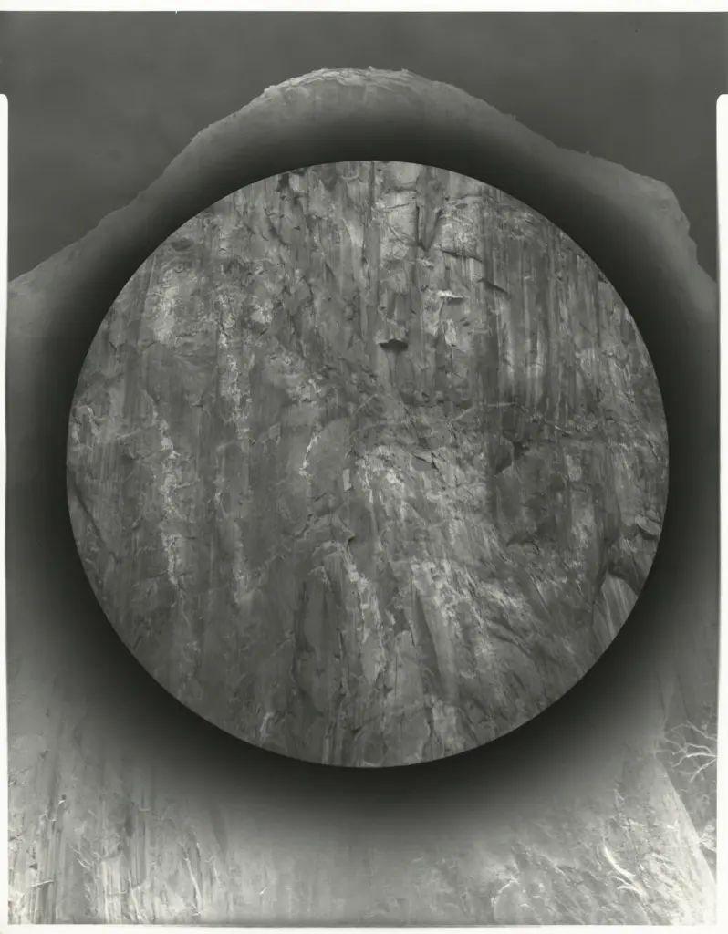 Black-and-white photographic work showing a circular, detailed view of a granite cliff within a darker negative-toned surround.